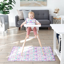 Load image into Gallery viewer, A smiling toddler in a high chair wearing a floral bib sits on a Bumkins Splat Mat: Watercolor, featuring stain-resistant fabric.
