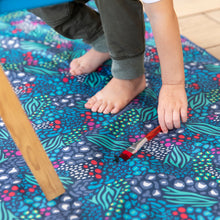 Load image into Gallery viewer, Close-up of a child reaching for a paintbrush on a Bumkins Splat Mat: Animal Prints, made of waterproof fabric for easy cleaning.