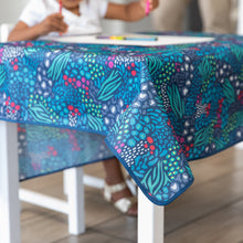 Load image into Gallery viewer, A child coloring at a table with a Bumkins Splat Mat: Animal Prints draped over the top.