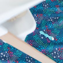 Load image into Gallery viewer, A silicone spoon with food rests on a Bumkins Splat Mat: Animal Prints underneath a high chair.