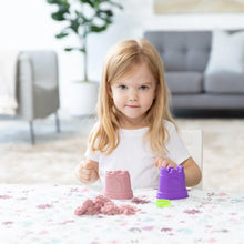 Load image into Gallery viewer, A girl plays with a purple sandcastle mold and kinetic sand on a Bumkins Splat Mat: Floral, with a plant and sofa in the background.