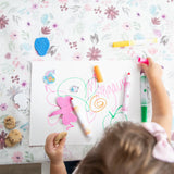 Aerial view of a child drawing with colorful pens on Bumkins Splat Mat: Floral, nibbling a cookie.