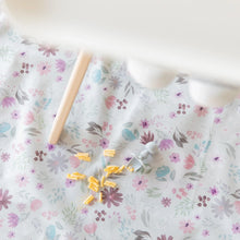 Load image into Gallery viewer, Bumkins Splat Mat: Floral lays under a high chair, covered in macaroni and cheese with a gray silicone utensil nearby.
