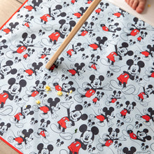 Load image into Gallery viewer, Food pieces sit on top of Bumkins Splat Mat: Mickey Mouse underneath a high chair with a child's food visible.