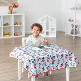 A child paints on Bumkins Splat Mat: Mickey Mouse covering a table in a bright room with toys on shelves.