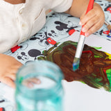 Close-up of a child painting with brown and green paint on paper on Bumkins Splat Mat: Mickey Mouse.
