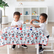 Load image into Gallery viewer, Two young children enjoy arts and crafts at a table covered by Bumkins Splat Mat: Mickey Mouse in a bright playroom.