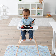 Load image into Gallery viewer, A baby in a high chair on the Bumkins Splat Mat: Mickey + Minnie Sunny Side Up joyfully uses a spoon in a toy-filled bright room.