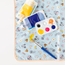 Load image into Gallery viewer, Blue and yellow paint tubes, a brush, and palette sit on a Bumkins Splat Mat: Mickey + Minnie Sunny Side Up on a white background.