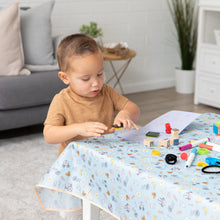 Load image into Gallery viewer, A toddler happily uses stamps and markers on a Bumkins Splat Mat: Mickey + Minnie Sunny Side Up in a plant-filled, cozy living room.