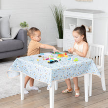Load image into Gallery viewer, Two children sit at a table covered with a Bumkins Splat Mat: Mickey + Minnie Sunny Side Up and art supplies in a cozy living room.