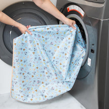 Load image into Gallery viewer, A person holds a Bumkins Splat Mat: Mickey + Minnie Sunny Side Up in front of an open front-loading washing machine.