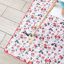 Load image into Gallery viewer, Scrambled eggs and a Mickey Mouse fork sit on a Bumkins Splat Mat: Minnie Mouse, under a wooden highchair leg on the floor.