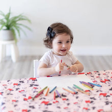 Load image into Gallery viewer, A toddler in a black bow draws with crayons at a table covered with Bumkins Splat Mat: Minnie Mouse.