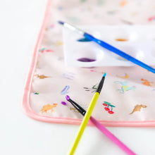 Load image into Gallery viewer, Close-up of three paintbrushes and a paint palette resting on Bumkins Splat Mat: Princess Magic on a white background.