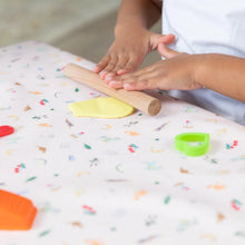 Load image into Gallery viewer, A child uses a wooden rolling pin to roll yellow clay on Bumkins Splat Mat: Princess Magic while cookie cutters sit close by.