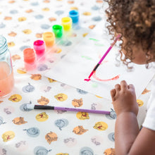 Load image into Gallery viewer, A child paints with watercolors at a table, with colorful paints and a water jar on Bumkins Splat Mat: Winnie and Friends for easy cleaning.