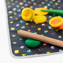 Load image into Gallery viewer, Close-up of Bumkins Splat Mat: Super Mario™ Lineup on a white background with a wooden rolling pin and open containers of play dough on top.