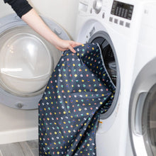 Load image into Gallery viewer, A person places Bumkins Splat Mat: Super Mario™ Lineup into an open front-loading washing machine.