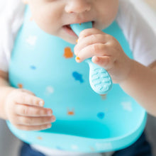 Load image into Gallery viewer, Close-up of a baby wearing a Bumkins Silicone Bib: Ocean Life, chewing on a blue spoon.