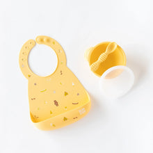 Load image into Gallery viewer, Bumkins Silicone Bib: Camp Gear lays on a white background next to a yellow bowl & spoon set.