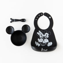 Load image into Gallery viewer, Bumkins Silicone Bib: Mickey + Minnie Mouse lays next to a black Mickey Mouse-shaped bowl & spoon set on a white background.