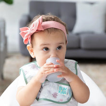Load image into Gallery viewer, A baby in a pink headband and floral bib drinks from a Bumkins Silicone Starter Cup: Gray in a high chair.