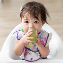 Load image into Gallery viewer, A girl in a floral bib sits in a high chair, drinking from a Bumkins Silicone Starter Cup: Sage.