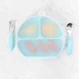 Bumkins Silicone Stretch Lid for Grip Dish 3 Section, Grip Plate covers a blue plate of food on a marble surface with blue utensils nearby.