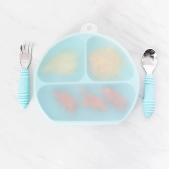 Bumkins Silicone Stretch Lid for Grip Dish 3 Section, Grip Plate covers a blue plate of food on a marble surface with blue utensils nearby.