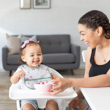 Load image into Gallery viewer, A smiling mom feeds a happy toddler in a high chair from a pink bowl; the toddler wears a Bumkins Starter Bib 2 Pack: Floral & Lace.