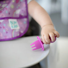 Load image into Gallery viewer, Close-up of a baby in a purple bib seated in a high chair holding a Bumkins Silicone Chewtensils®: Fuchsia.