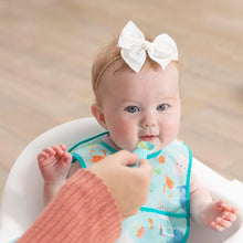 Load image into Gallery viewer, A baby in a Bumkins Starter Bib 2 Pack: Ocean Life & Whale Tail sits in a high chair, being spoon-fed by an adult hand.
