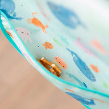 Load image into Gallery viewer, Close-up of a Bumkins Starter Bib 2 Pack: Ocean Life & Whale Tail with pretzels in the pocket.
