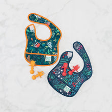 Load image into Gallery viewer, Bumkins Silicone Chewtensils®: Red rests on top of a animal print bib on a marble surface next to another similar bib and orange utensils.