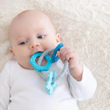 A baby lies on a beige blanket in a white onesie, chewing a Bumkins Silicone Teething Charms: Blue.