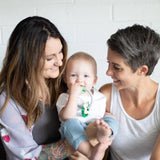 Two women smile at a baby chewing a Bumkins Silicone Teething Charms: Green.