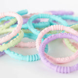 Multiple sets of Bumkins Silicone Teething Rings 4 Pack: Spring in a pile on a white background.