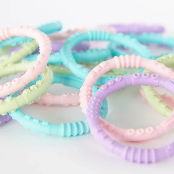 Multiple sets of Bumkins Silicone Teething Rings 4 Pack: Spring in a pile on a white background.