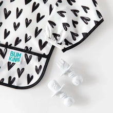 Load image into Gallery viewer, Close-up of Bumkins Sleeved Bib: Hearts next to marble toddler utensils on a white background.