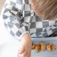 Load image into Gallery viewer, Close-up of a child practicing baby-led weaning, enjoying small pancakes while wearing a Bumkins Sleeved Bib: Charcoal Check.