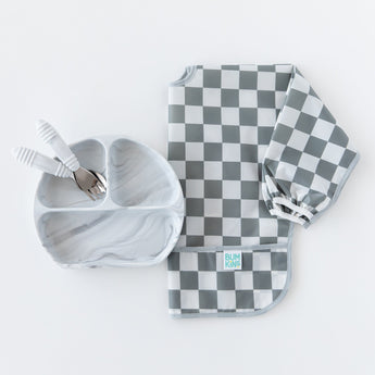 Bumkins Sleeved Bib: Charcoal Check is displayed with a gray divided plate and matching utensils on a white background.