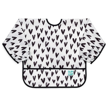 Bumkins Sleeved Bib: Hearts is a white waterproof bib with a black heart pattern, black trim, front pocket, and long sleeves.