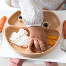 Load image into Gallery viewer, Close-up of a child's hand reaching for orange slices on a plate with cottage cheese and snacks, while wearing a Bumkins Sleeved Bib: Wander.