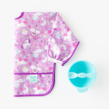 Load image into Gallery viewer, Bumkins Sleeved Bib: Unicorns lays folded next to a blue bowl & spoon set on a white background.
