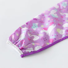 Load image into Gallery viewer, Close-up of Bumkins Sleeved Bib: Unicorns on a white background with focus on the elastic cuff on the sleeve.