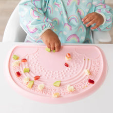 Load image into Gallery viewer, Close-up of a baby in a Bumkins Sleeved Bib: Rainbows playing with food on a pink silicone placemat.