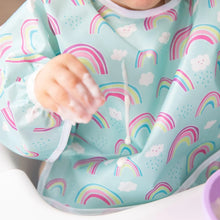 Load image into Gallery viewer, Close-up of a child in a Bumkins Sleeved Bib: Rainbows with a drop of yogurt spilling down the front of the bib.