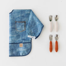 Load image into Gallery viewer, Bumkins Sleeved Bib: Vintage Denim lays folded next to two sets of silicone-handled utensils on a white background.