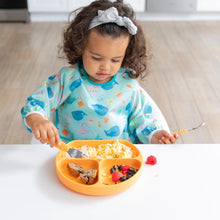 Load image into Gallery viewer, A toddler enjoys scrambled eggs, fruit, and bread from an orange divided plate while wearing a Bumkins Sleeved Bib: Ocean Life.